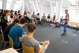 Žáci sedí v kruhu na židlích.