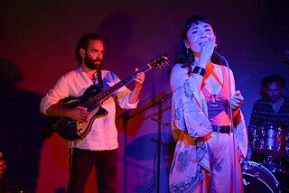 Timothy Daniel ist links im Bild an der E-Gitarre zu sehen, rechts vor ihm steht die singende Elaha Soroor. Hinten rechts ist der Schlagzeuger Stefano Ancoro zu erkennen.