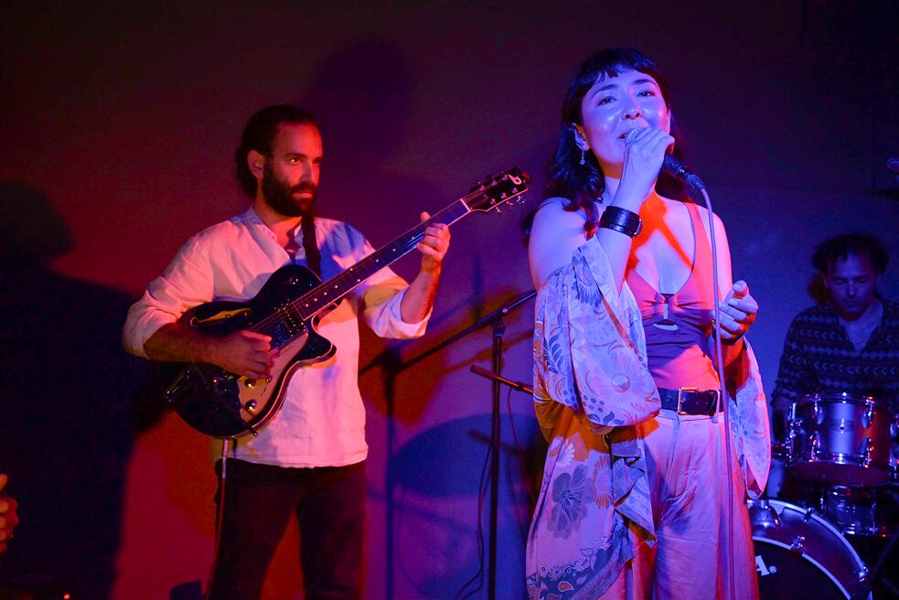 Timothy Daniel ist links im Bild an der E-Gitarre zu sehen, rechts vor ihm steht die singende Elaha Soroor. Hinten rechts ist der Schlagzeuger Stefano Ancoro zu erkennen.
