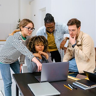 Eine Gruppe junger Menschen, die über einem Laptop diskutieren.