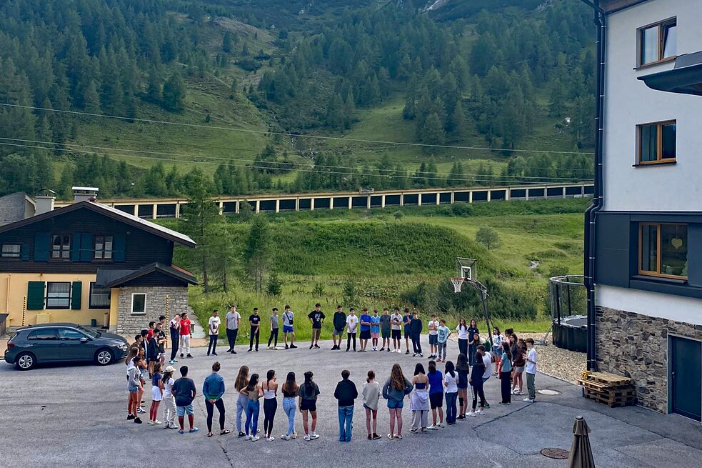 Kinder stehen in einem Kreis auf einem gepflasterten Hof.