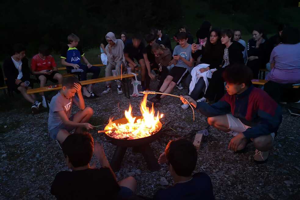 Jugendliche am Lagerfeuer halten Stockbrot über das offene Feuer.