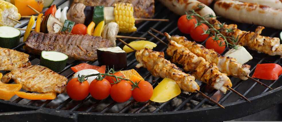 Gemüse, Fleisch und Würtchen liegen auf einem Grill.