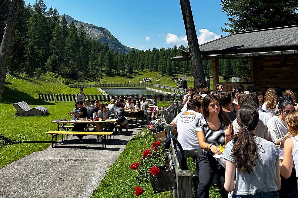 Jugendliche sitzen an langen Tischen und essen zu Mittag. Die Sonne scheint.