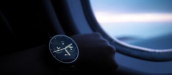 Eine Smartwatch an einem jugendlichen Arm vor einem Fenster in einem Flugzeug.