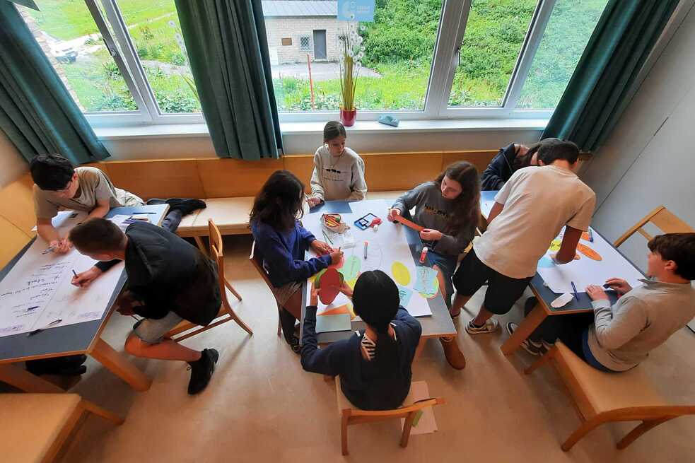 Jugendliche sitzen an niedrigen Tischen und malen.