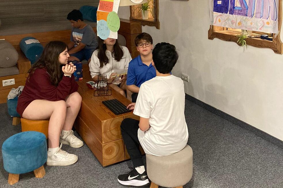 Jugendliche sitzen auf Hockern an einem niedrigen Tisch