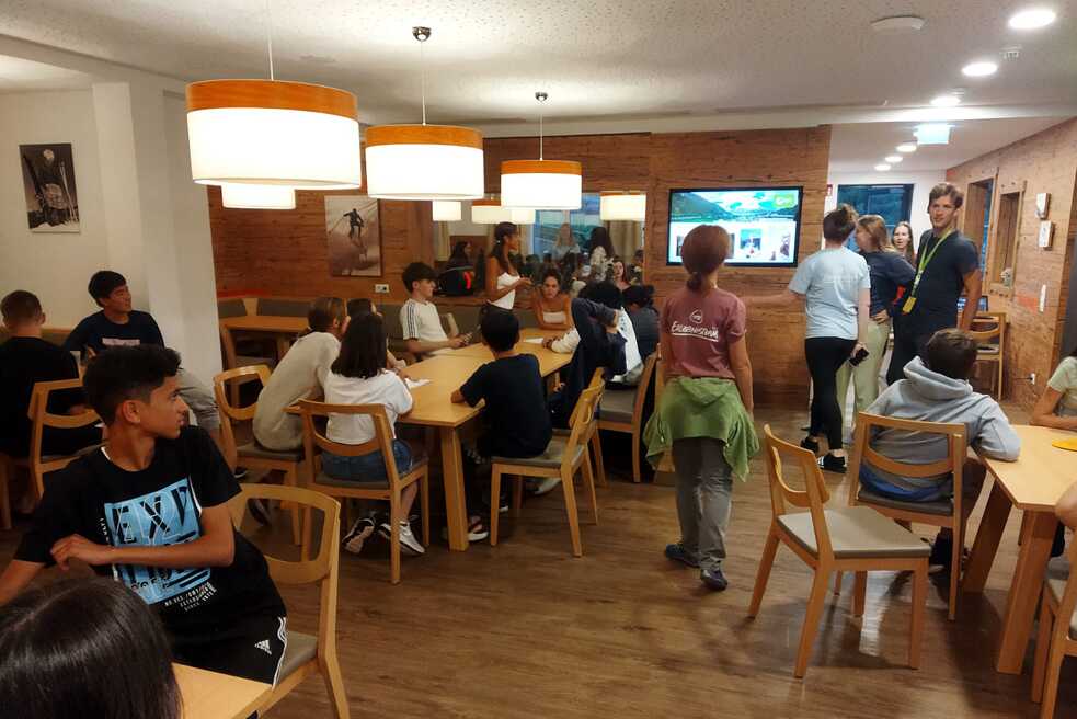 Jugendliche sitzen in kleinen Gruppen an Tischen.