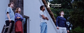 Quatre jeunes gens (une jeune fille, trois jeunes hommes) debouts devant la partie superieure d'un batiment, regardent le iel, leur regard est inquiet. Au premier plan le haut d'une echelle posée contre ce batiment