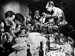 Filmstill aus „Kuhle Wampe oder Wem gehört die Welt?”, das eine Gruppe von Personen zeigt, die an einem Tisch miteinander essen