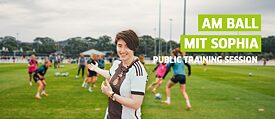 WM Reporterin im Deutschlandtrikot vor trainierenden Fußballerinnen