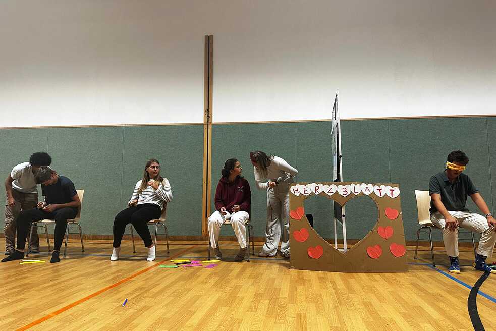 Jugendliche spielen die Sendung „Herzblatt“ in einer Turnhalle nach.