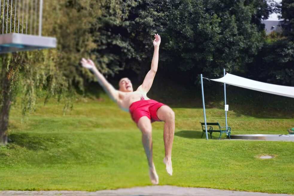 Ein junger Erwachsener spring von einem Turm in einen Pool.