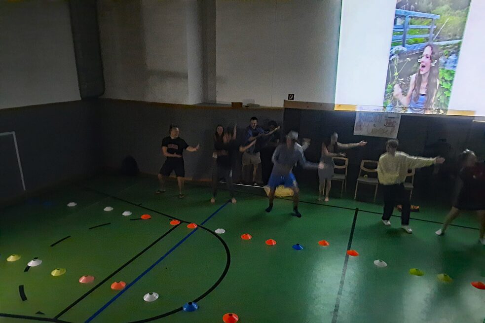 In einer dunklen Sporthalle tanzen Jugendliche, hinter ihnen die Projektion eines Fotos an der Wand.