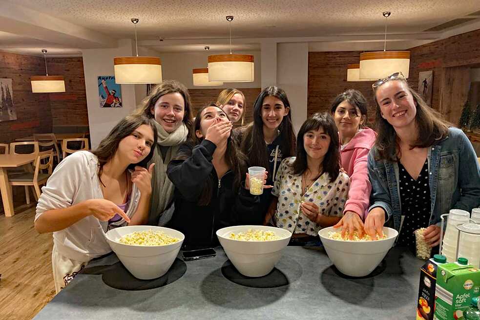 Junge Mädchen stehen an einem Tisch und genißen frischen Popcorn.