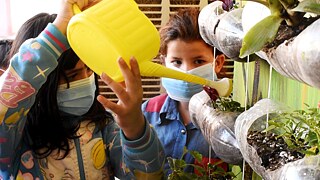 Kinder gießen einen vertikalen Garten aus recycelten Plastikflaschen
