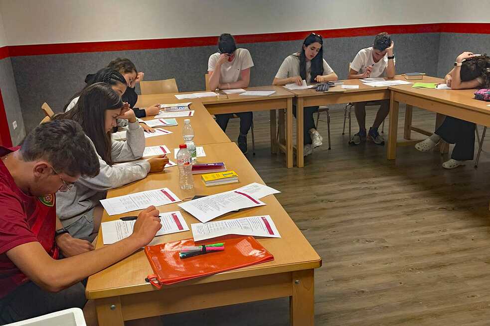 Jugendliche an in U-Form aneinander gereihten Tischen blicken konzentriert auf Arbeitsblätter.