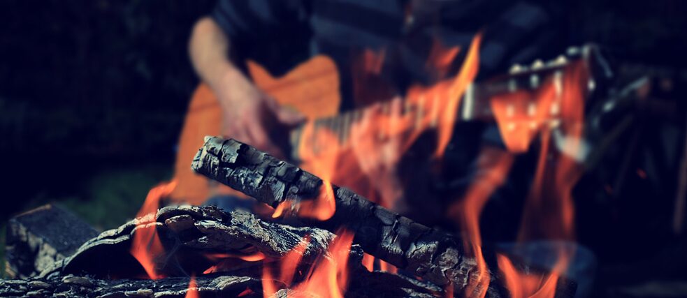 Jemand spielt Gitarre am offenen Lagerfeuer.