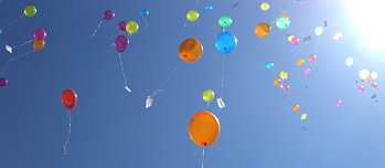 Luftballons mit Wunschzetteln am blauen Himmel