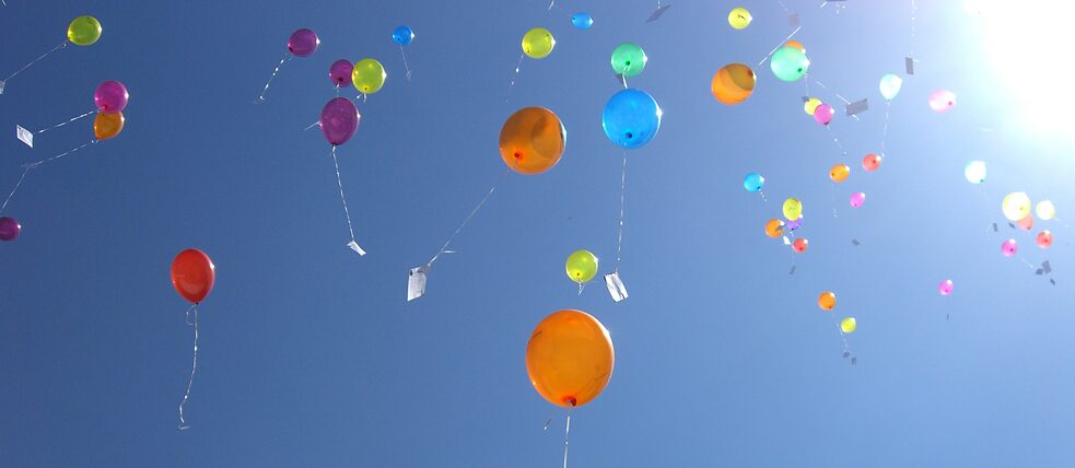 Luftballons mit Wunschzetteln am blauen Himmel