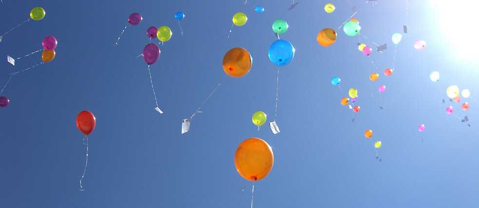 Luftballons mit Wunschzetteln am blauen Himmel