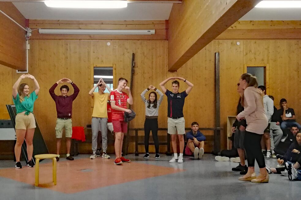 Jugendliche in einem Raum halten die Hände über dem Kopf.