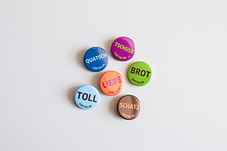 6 badges in light blue, dark blue, purple, brown, orange and green with the German words Quatsch, toll, Liebe, tschüss, Btor and Schatz on it.  © ©Jayne Lloyd/Goethe-Institut London Badges