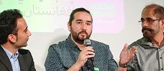 Omaid Sharifi spricht zum Publikum während der Moderator Saeed Shinwari und Rahraw Omarza ihm aufmerksam zuhören.