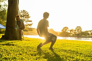 Ein Mann und eine Frau auf einer Slackline im Grünen