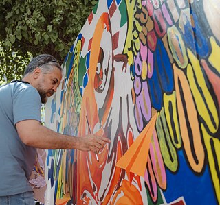 Artist Kabir Mokamel works standing on a colorful street art piece.