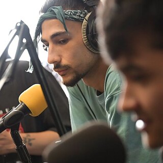 Ein Mietglied der Gruppe Ak13 beugt sich während eines Radio-Interviews zum Mikrofon.