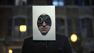 André Breton (played by Louis-Do de Lencquesaing), one of the Surrealist movement’s founders wearing goggles and a rectangle of paper framing his face.  Production Still from "Transatlantic"