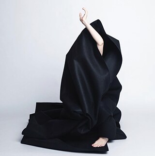 A dancer's hand emerges from a black mountain of fabric