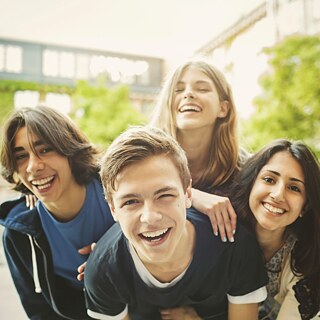 Vier junge Teenager blicken lachend in die Kamera.