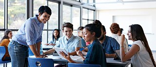 Lehrerin spricht im Klassenraum lächelnd mit einer Gruppe von Schülern