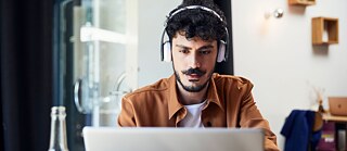 A young man is sitting at a table. In front of him is a laptop.