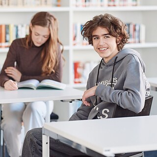 Молодой человек сидит за столом в библиотеке
