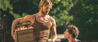A man standing holding a basket, another one next to him sitting in a natural environment