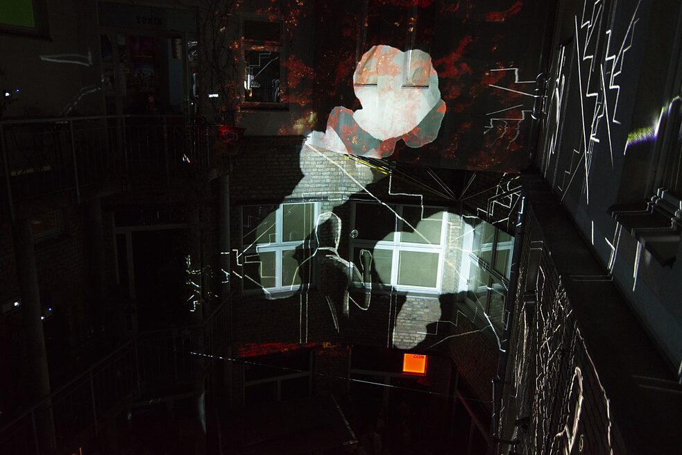 Mit Beamern wurden Bilder auf die Wände des Innenhofes projiziert. Die Zeichnung eines Mannes ist zu sehen und Gebäude, die in Flammen stehen.