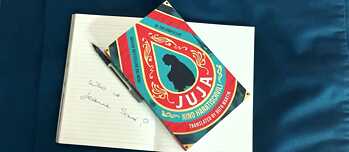 Neben der Notiz 'Who is Jeanne Saré? liegt das Buch 'Juja' und ein Kugelschreiber