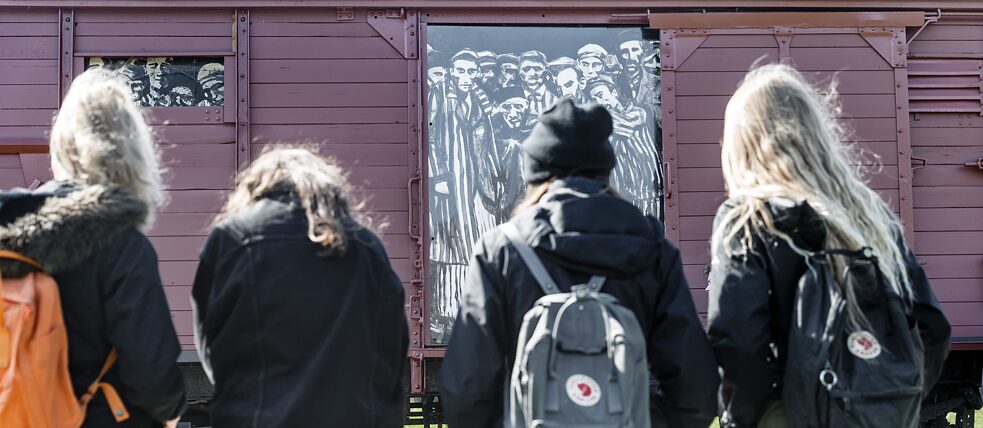 תלמידים מתבוננים בקרון רכבת היסטורי, המסמל את תחנת הרכבת לשעבר של מחנה הריכוז נוינגמה. 
