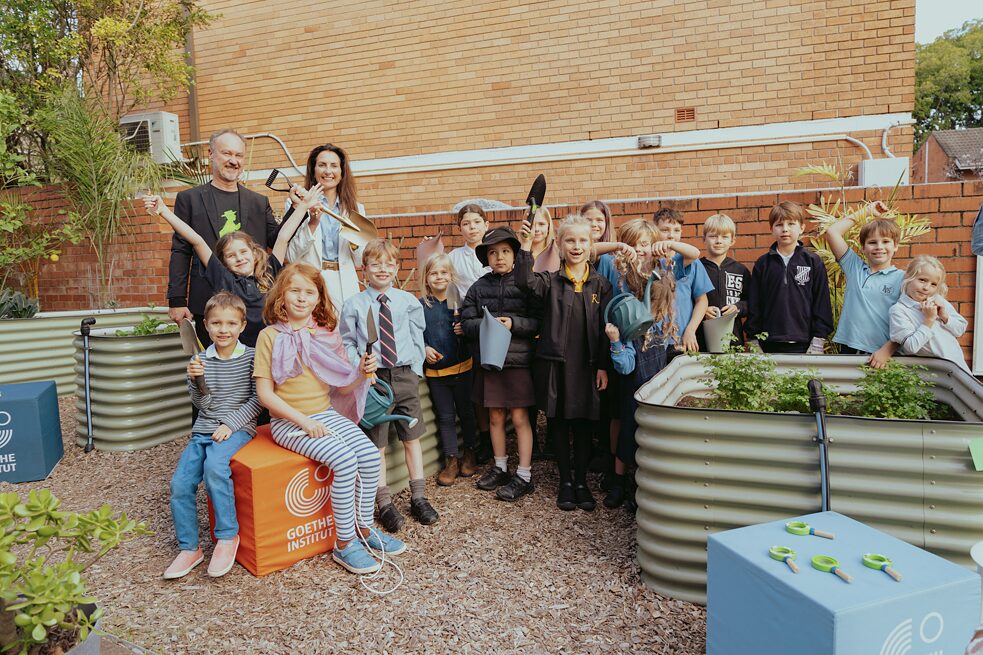 A school class stands next to a flower bed and proudly presents their work