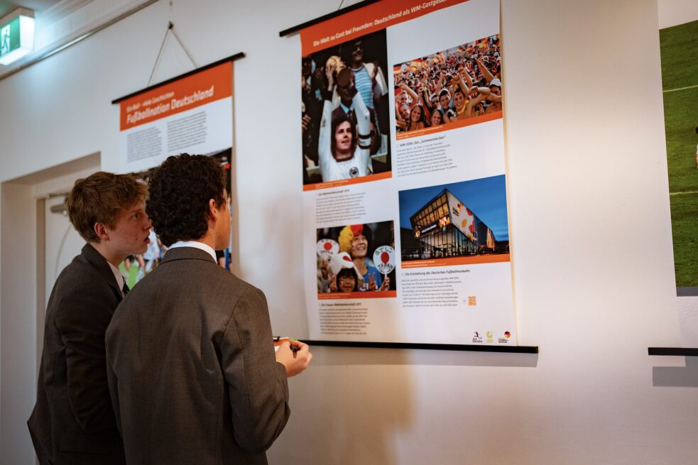 2 students stand with their backs to the camera and look at a poster about soccer