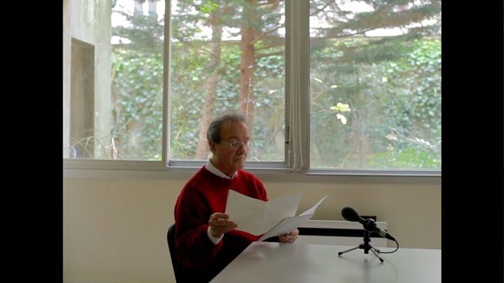 Eine männliche Person sitzt an einem Schreibtisch mit einem Mikrophon