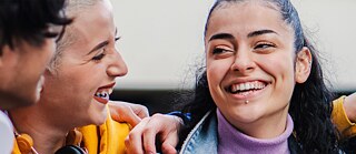 Drei junge Menschen lachen und haben die Arme umeinander gelegt