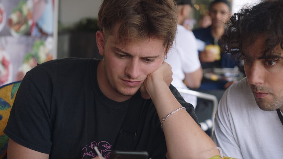 Junger Mann hält einen Stift in der Hand und schaut nachdenklich nach unten.