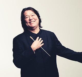 Der Dirigent Joseph Swenson in schwarzer Kleidung vor hellem Hintergrund.