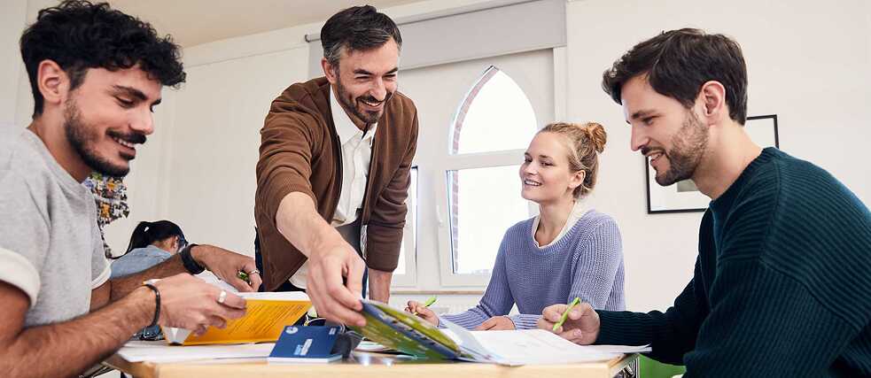 A teacher smiles as he recommends learning materials to a group of learners.