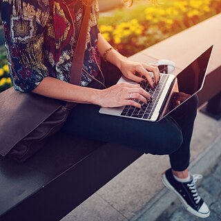 Eine junge Frau sitzt im Park mit Laptop