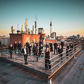 Singers stand on a roof terrace with the Berlin TV tower in the background